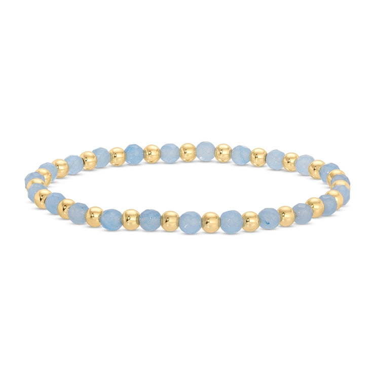 A beaded stretch bracelet featuring faceted light blue beads and polished gold spacer beads, arranged in a circular shape on a clean white background.