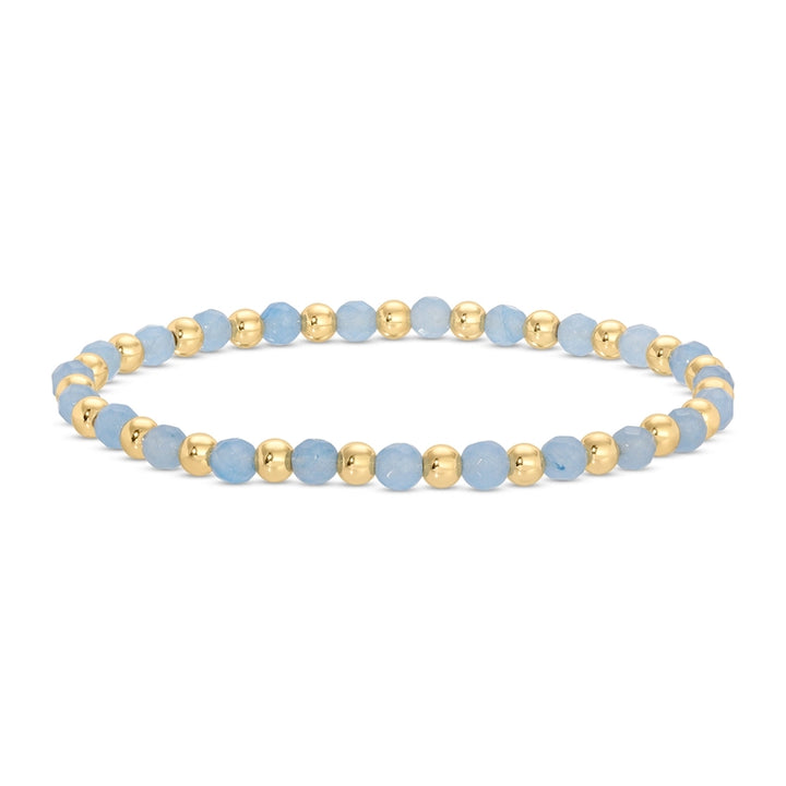 A beaded stretch bracelet featuring faceted light blue beads and polished gold spacer beads, arranged in a circular shape on a clean white background.
